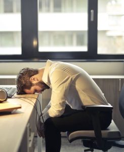 A person slumped over in her chair, head on desk exhausted after his motivation has diminished. Representing the self-improvement lie.